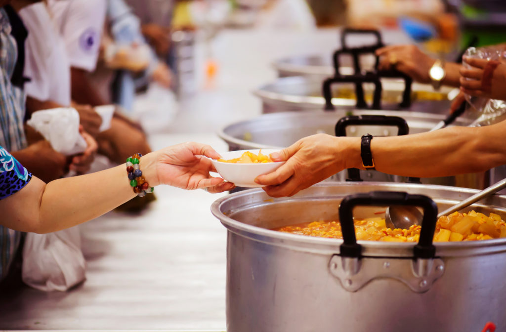 Person being handed a bowl of food a soup kitchen.