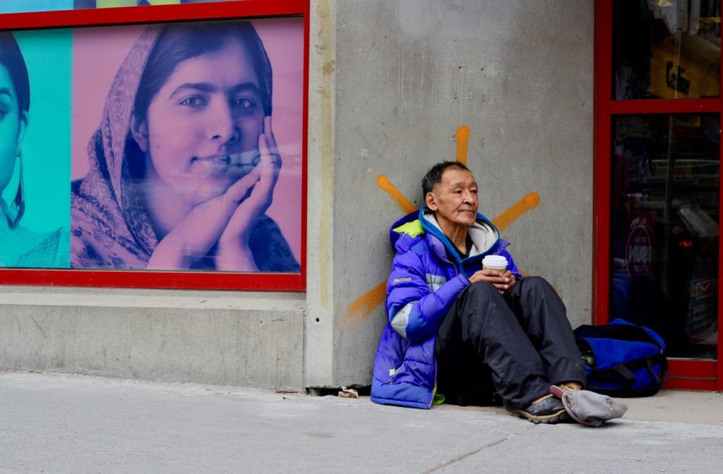 Homeless man sitting on a sidewalk with a coffee