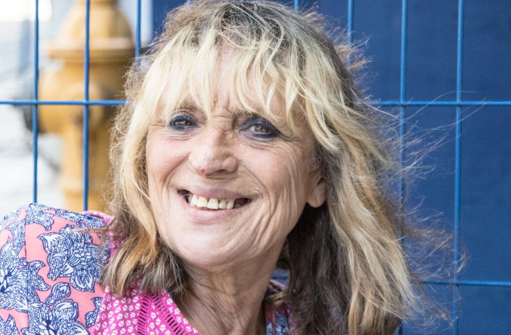 Woman experiencing homelessness smiling while leaning against metal fence
