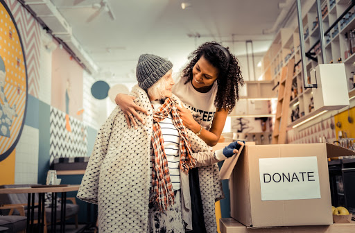 Woman helping another woman find clean clothes in donation box