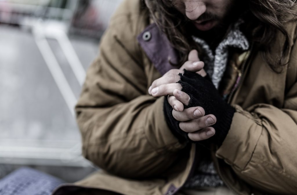 Cold homeless man wearing gloves to stay warm.