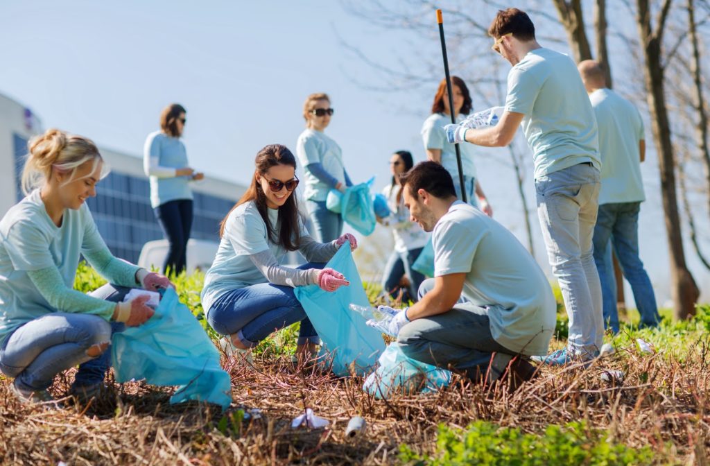 Happy volunteers helping clean the community by picking up trash on a sunny day.