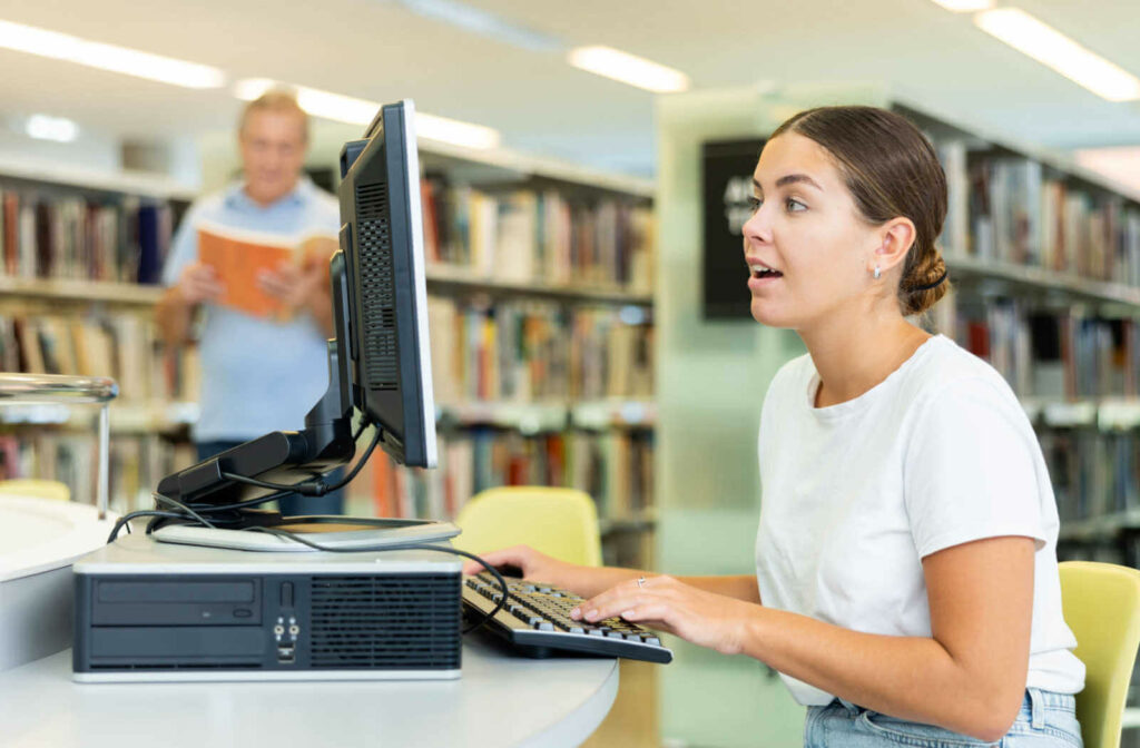 A young woman sitting in front of a computer in a public library is searching for jobs online.