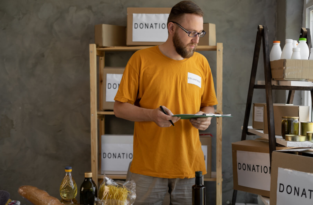 A food bank volunteer checking the food donations they have received while holding a clipboard.