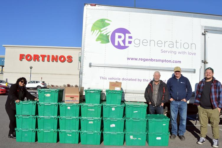 Volunteers stand in front of a regeneration cube van which is parked in a Fortinos parking lot. there are many green bins of food that teh volunteers are picking up