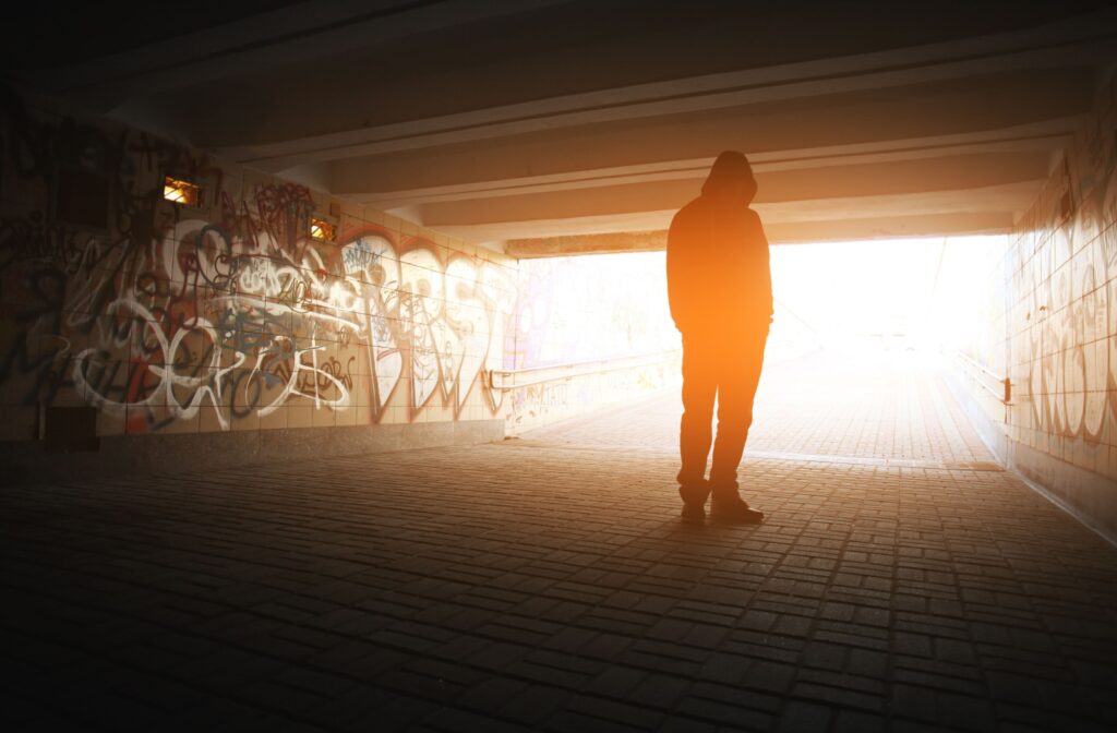 A person standing in a tunnel with their hood up and the sunlight shining towards them.