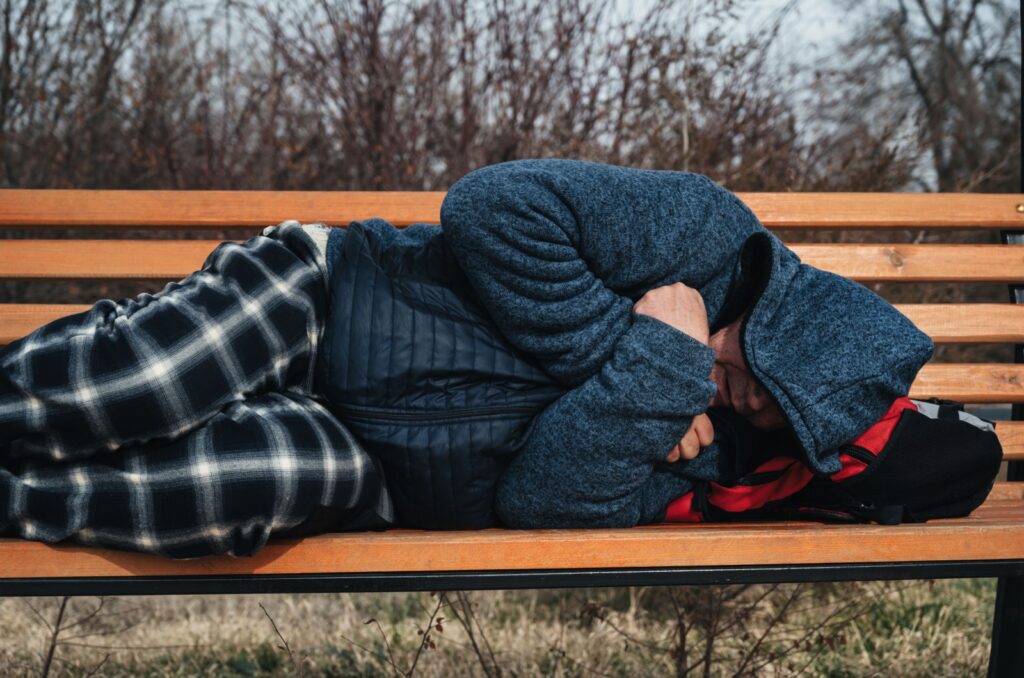 An individual experiencing homelessness sleeping on a park bench.