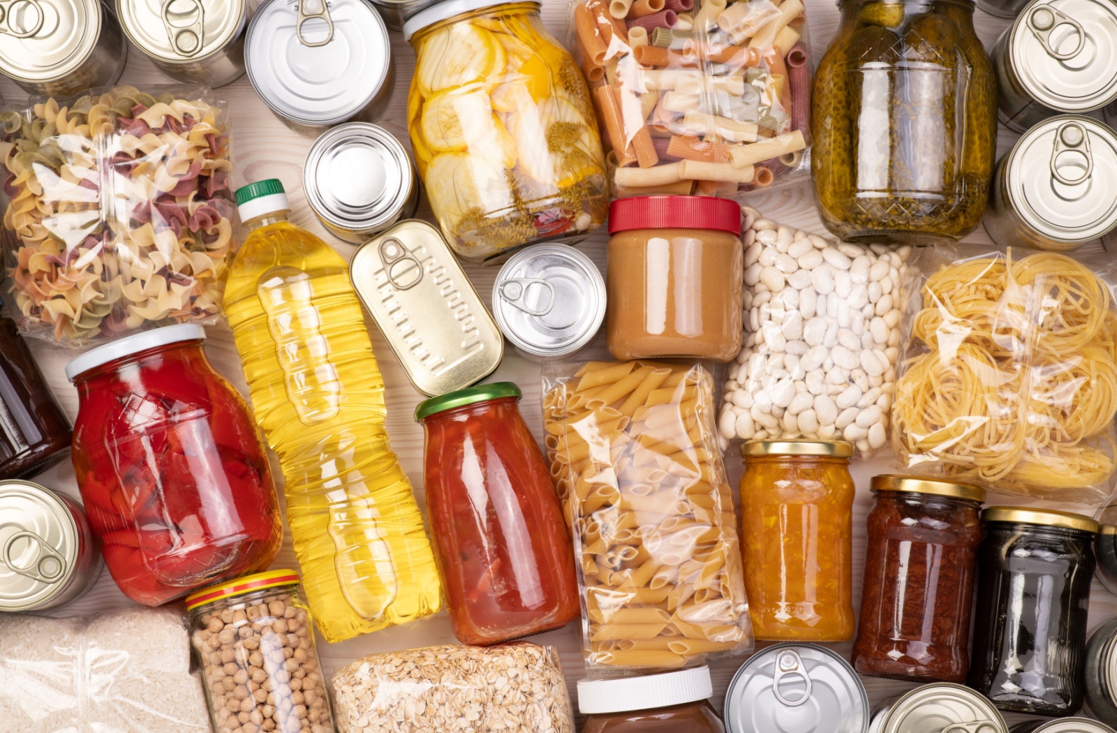 A table full of non-perishable food bank donations is shown. The items include several cans and bags of pasta as well as some jars of sauces and peanut butter.