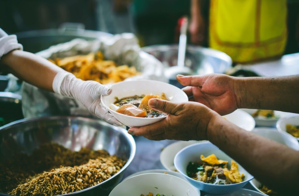 A close-up image of someone passing a bowl with a hot meal to a hungry person.